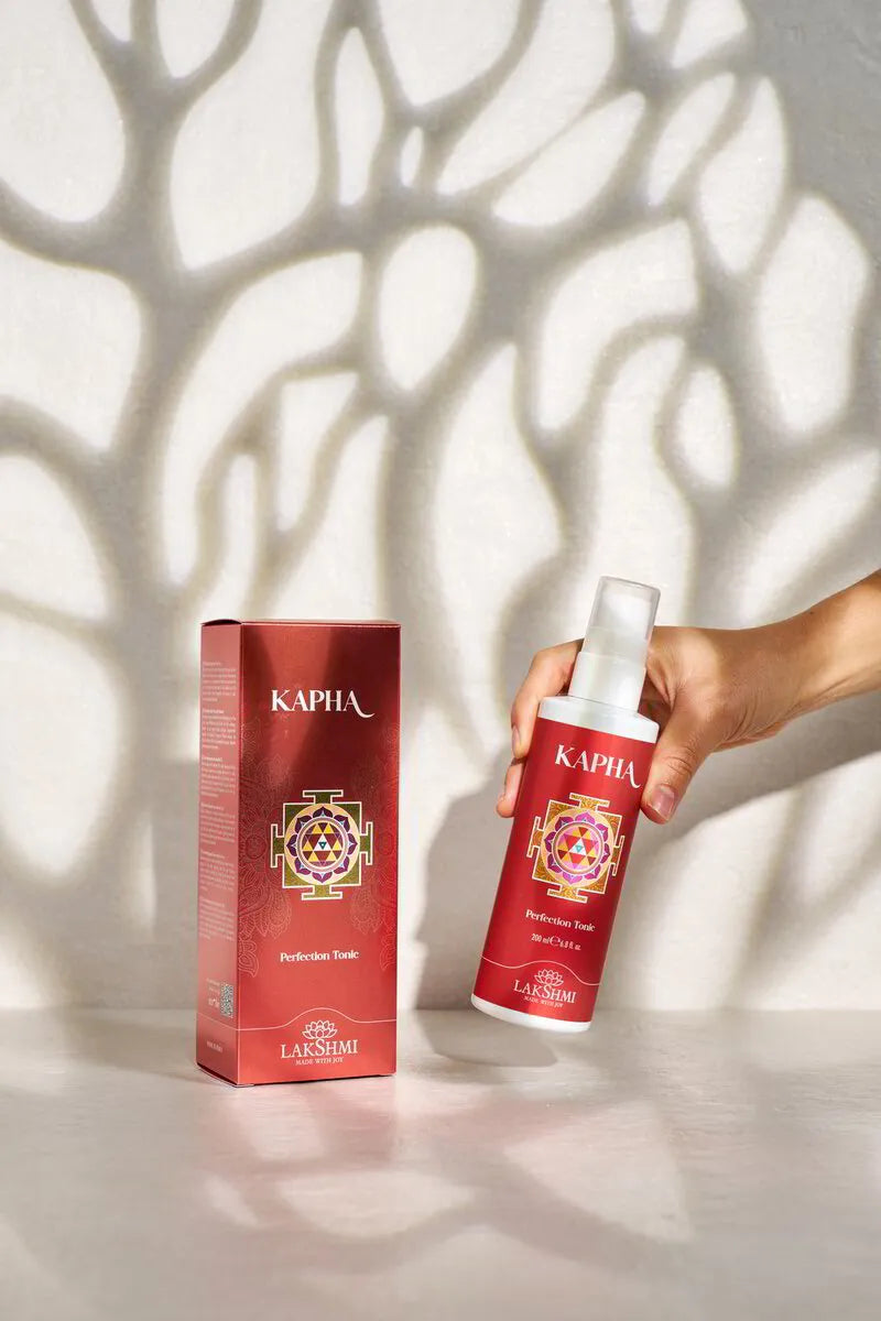 Hand lifting the Lakshmi KAPHA Perfection Tonic bottle from beside its box