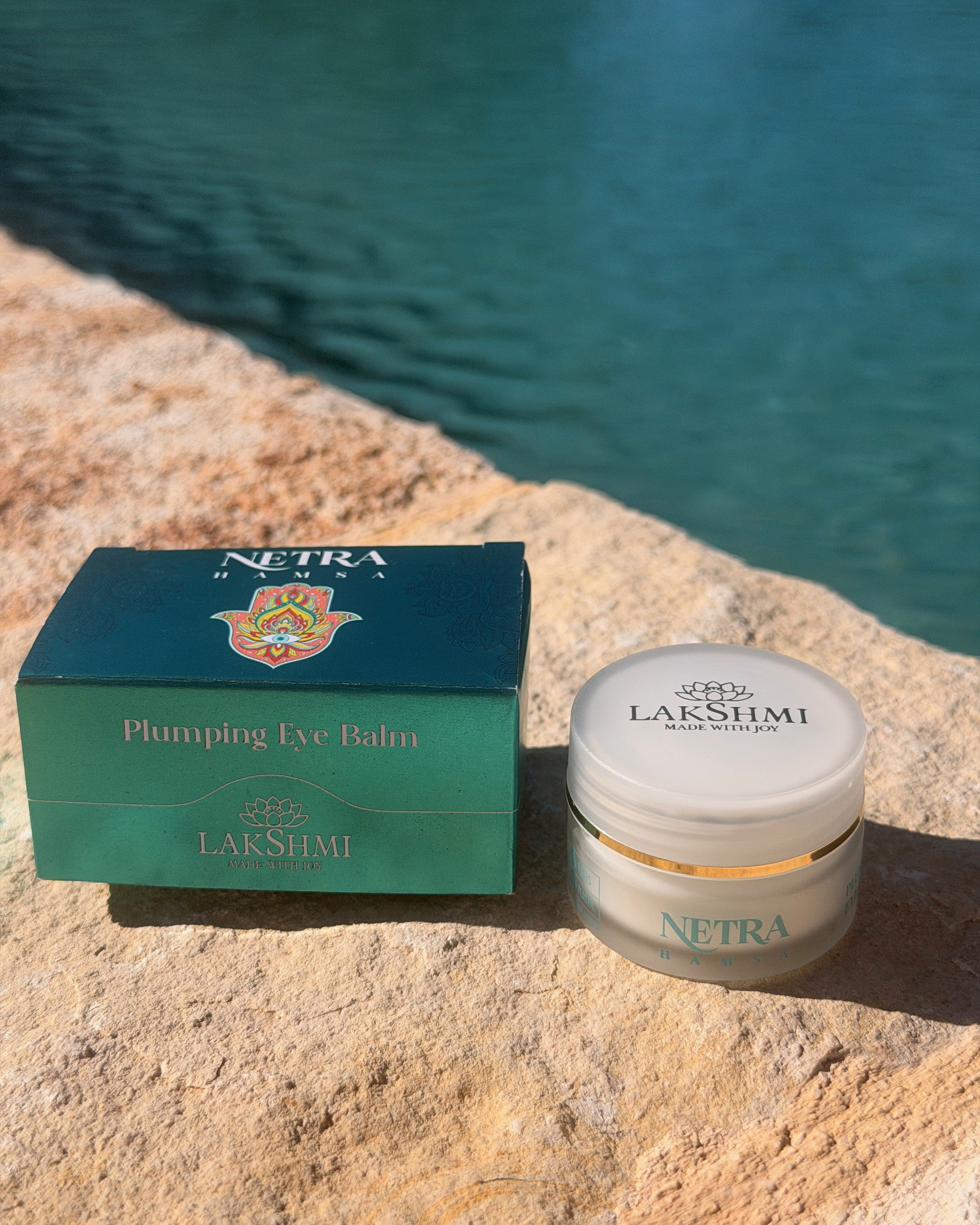 Lakshmi NETRA Plumping Eye Balm box and jar on stone by water