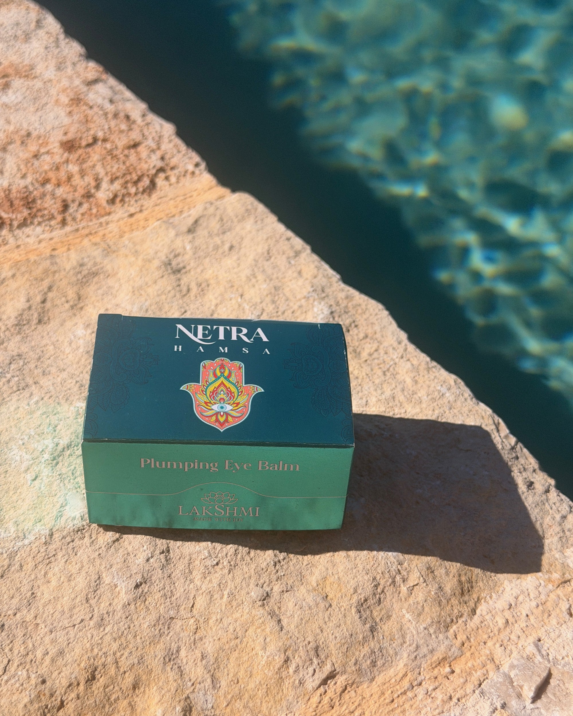 Lakshmi NETRA Plumping Eye Balm box beside a pool
